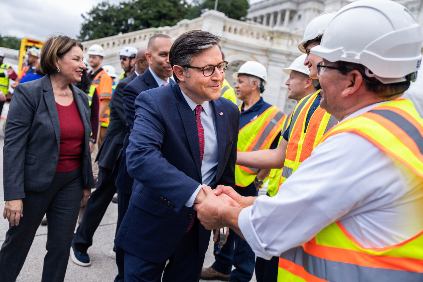 Speaker Mike Johnson, R-La., Sen. Amy Klobuchar, D-Minn., and House Minority Leader Hakeem Jeffries, D-N.Y., background, greet Architect of the Capitol workers during the “first nail ceremony,” marking the start of construction of the inauguration platform on the West Front plaza of the Capitol on Wednesday.