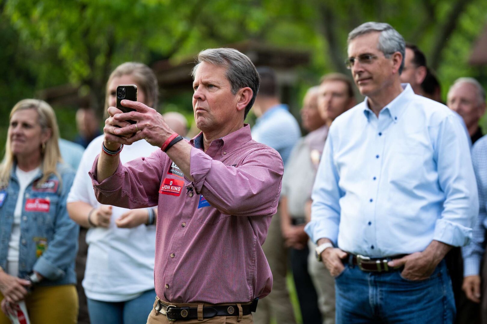 Gov. Brian Kemp takes a photo as Georgia Secretary of State Brad Raffensperger looks on at an annual cookout in Glennville, Ga., in April. Kemp is expected to defeat former Sen. David Perdue — former President Donald Trump's pick — this week in the GOP gubernatorial  primary.