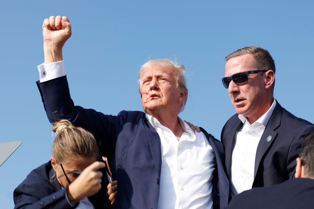 Former President  Donald Trump raises his fist as he is taken, with blood on his face, from the stage at a rally in Butler, Pa. on Saturday.