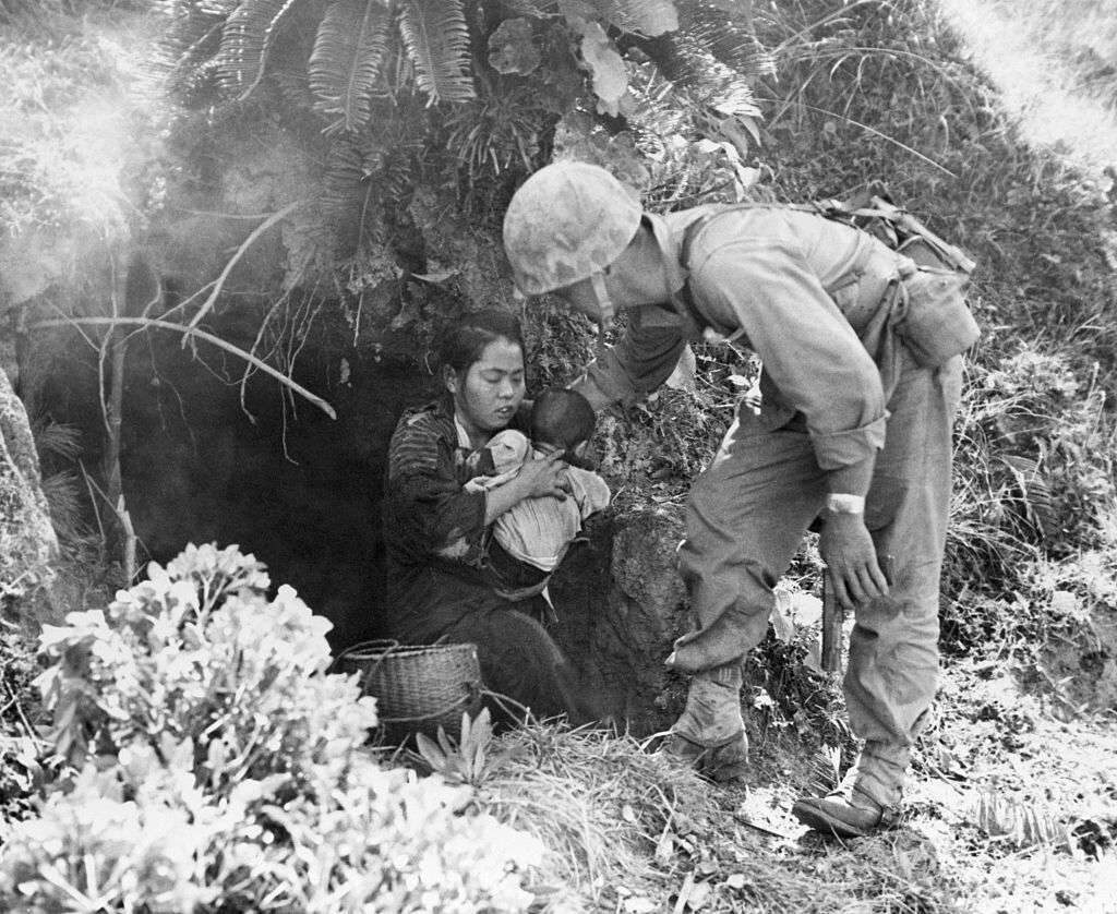 Eleven Okinawan civilians who were huddled in this hillside cave in 1945 were rescued when a passing U.S. Marine patrol heard a baby crying. After being assured that no harm would come to them, they emerged from their hideout, and here a Marine lends a hand to a mother and baby.